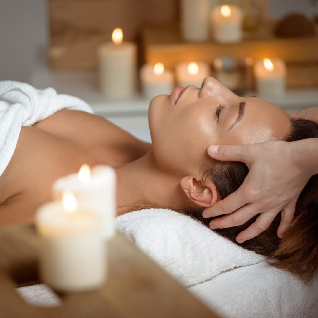 Young beautiful brunette girl having face massage relaxing in spa salon. Eyes closed. Copy space.